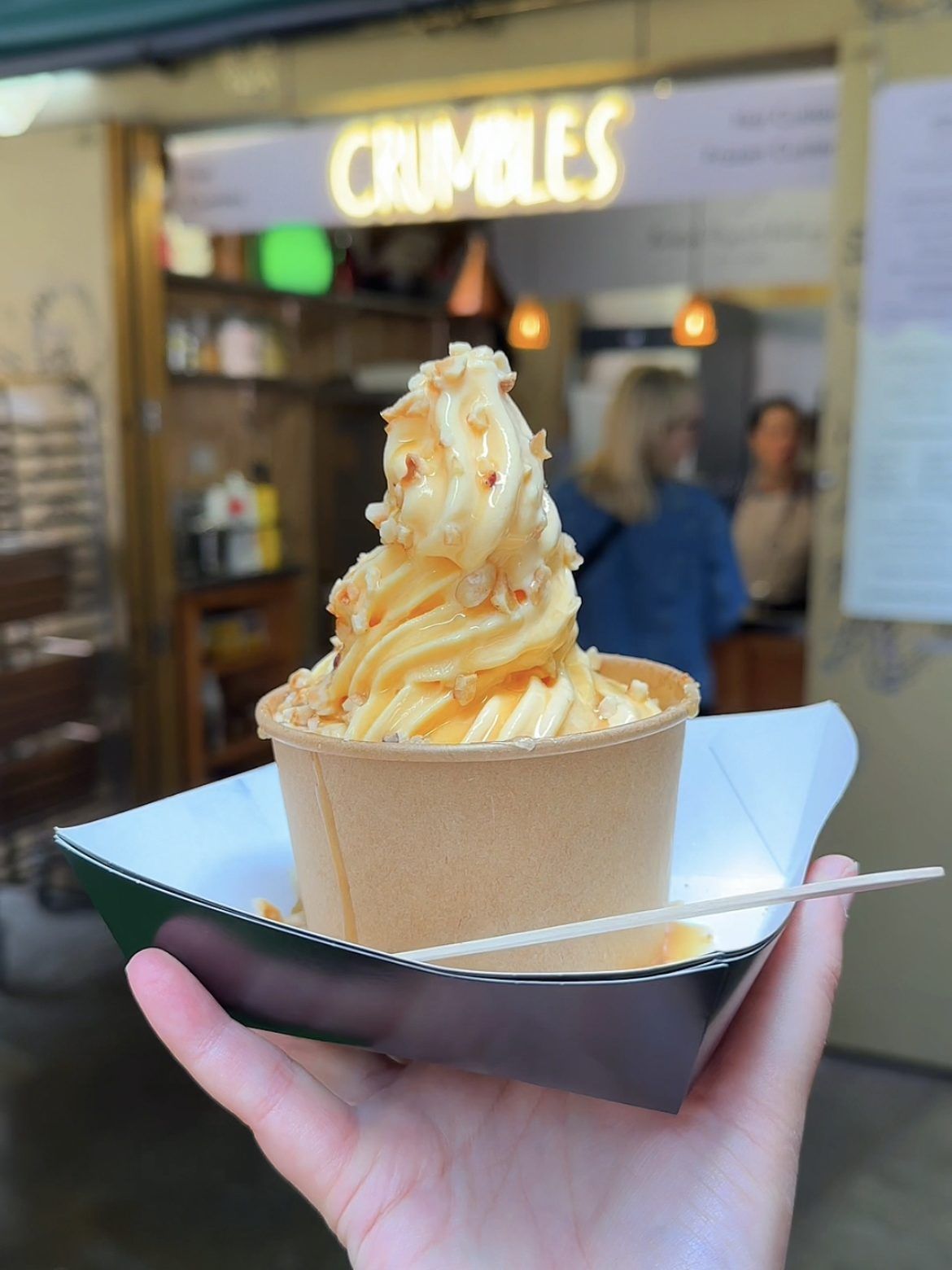 Hand holding a dessert cup with swirled soft serve and caramel topping; 