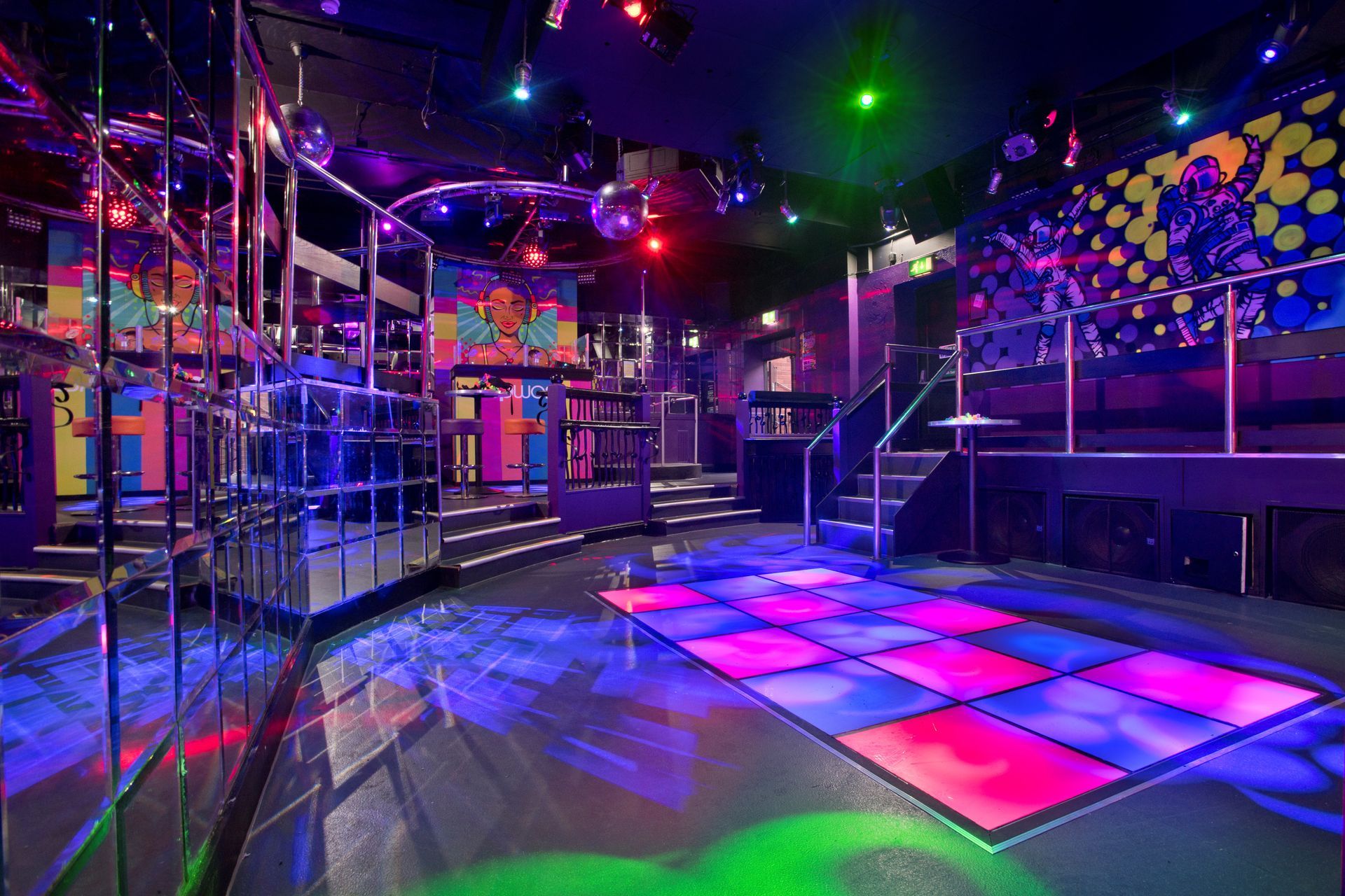 Empty, brightly lit nightclub with checkered dance floor and disco ball.