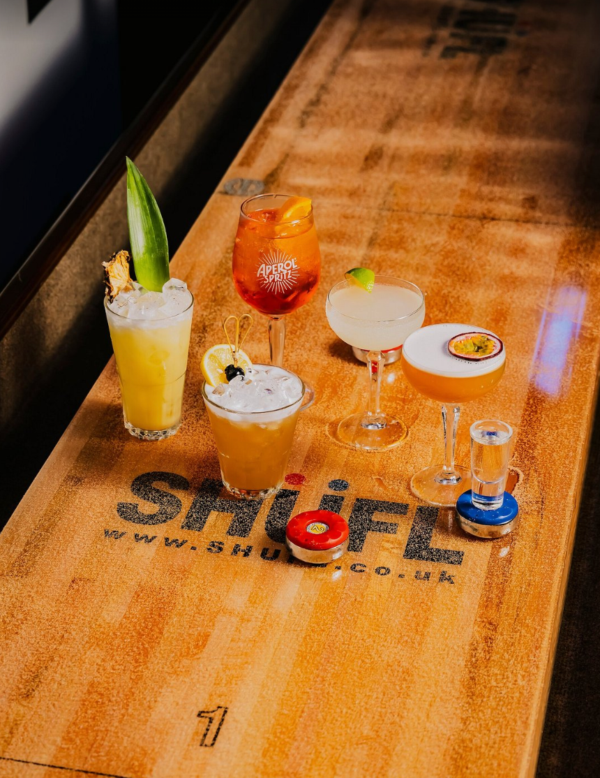 Cocktails on a wooden shuffleboard table, with shuffle pucks.