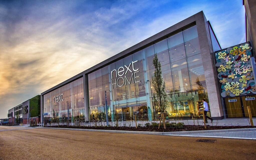 Next Home store exterior, modern glass facade, sign, cloudy sky.