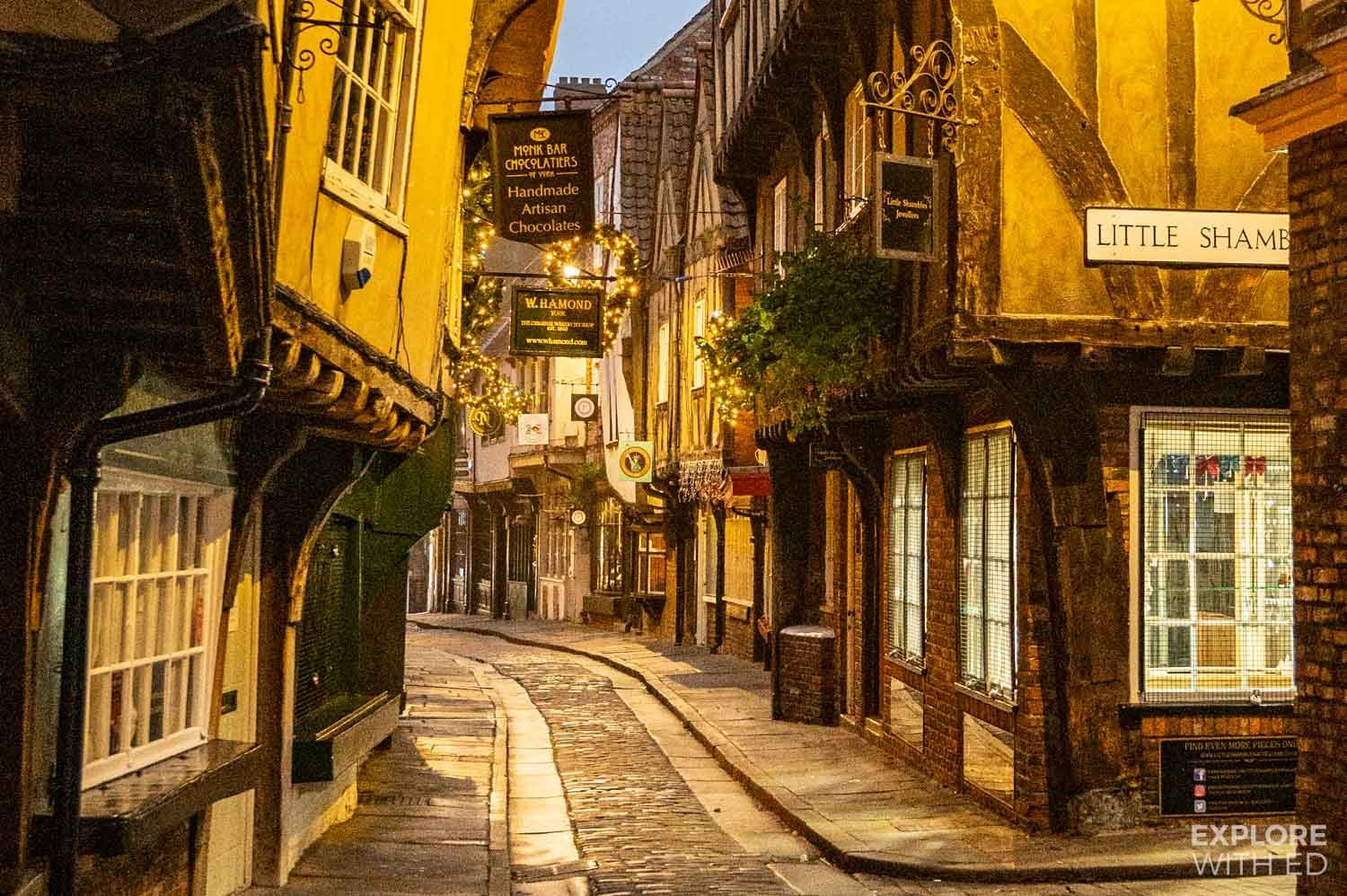 Cobblestone street in York, England, lined with historic buildings, illuminated by warm light at dusk.