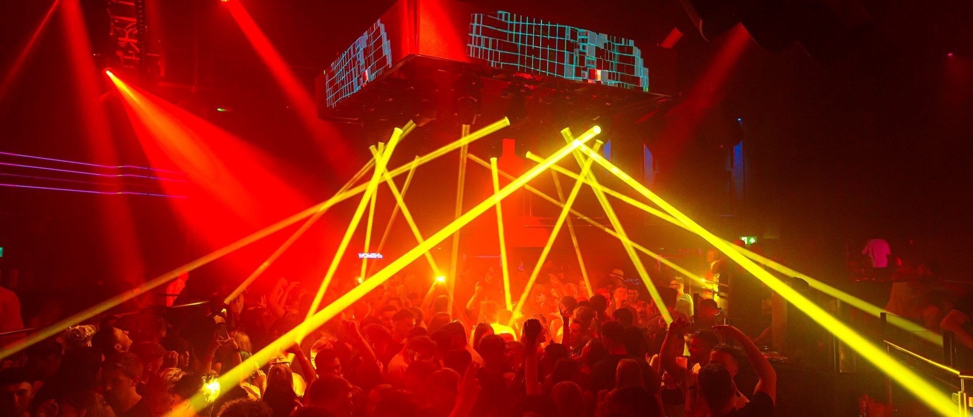 A concert with bright red and yellow stage lights shining on a crowd.