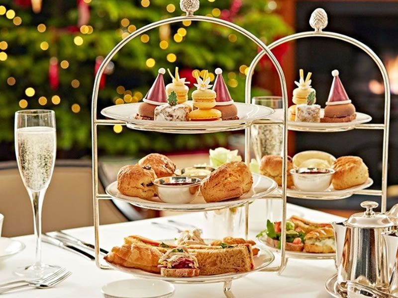 Christmas afternoon tea, tiered tray with festive sweets and scones, champagne, tree background.