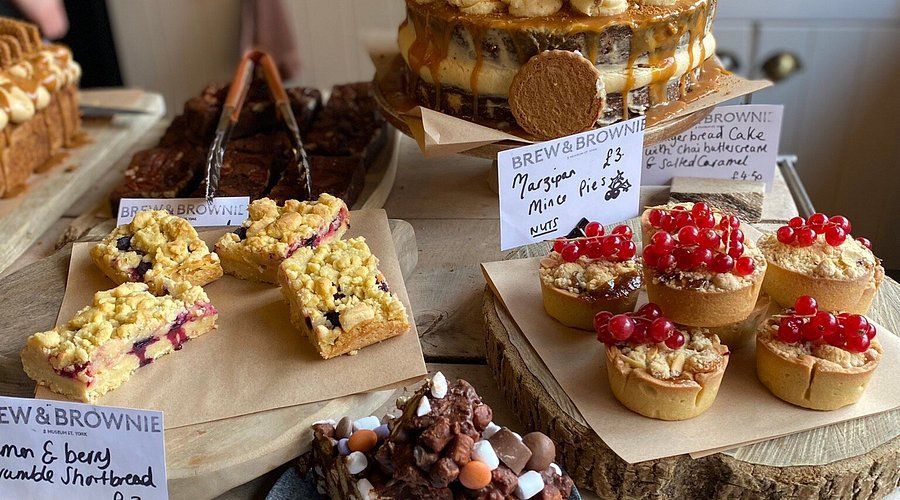 Baked goods display: cakes, tarts, and squares on a wooden table with handwritten price tags.
