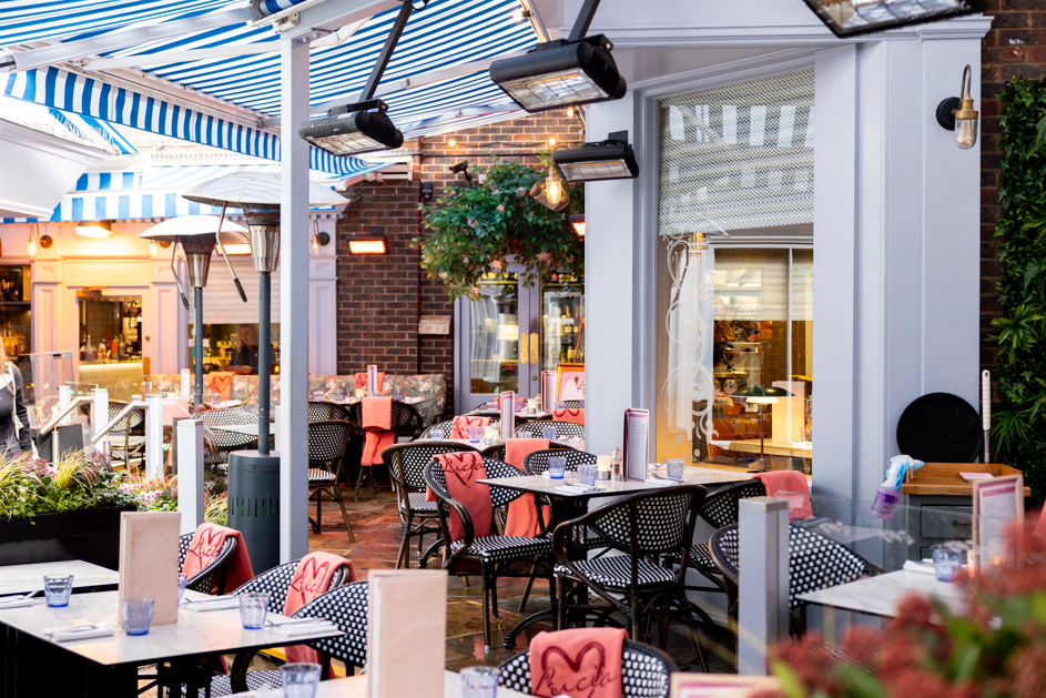 Outdoor restaurant patio with tables, chairs, heaters, and blue-striped awning.