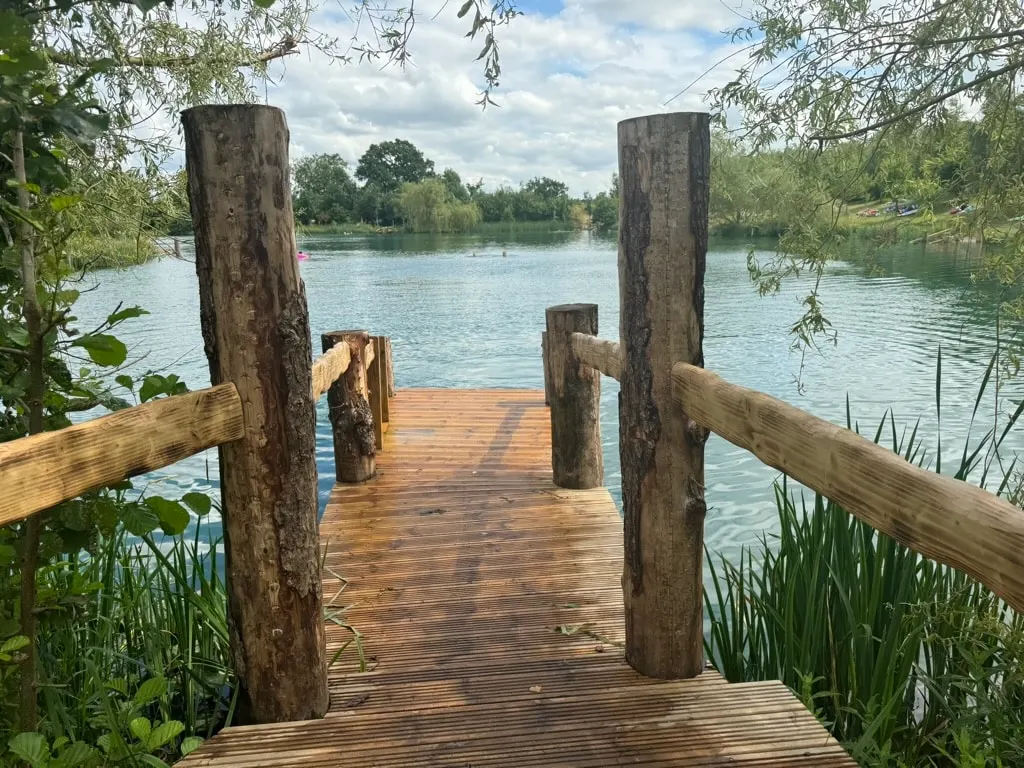 A wooden dock leading to a lake with trees in the background.