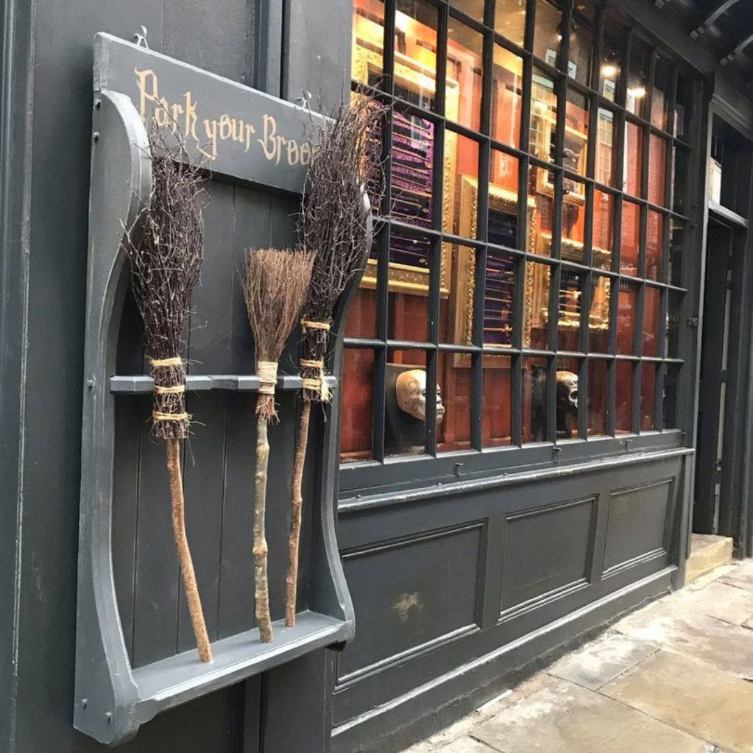 A broom parking rack with brooms, next to a shop window. Sign says 