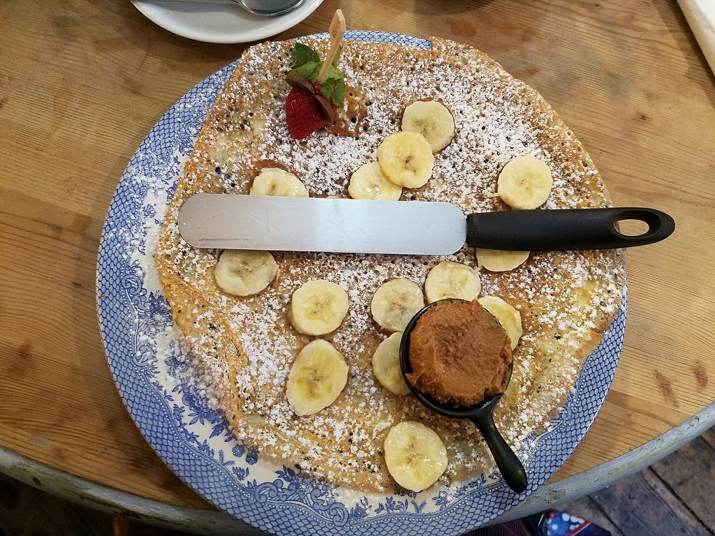 A pancake with bananas and powdered sugar on a blue and white plate with a spatula.