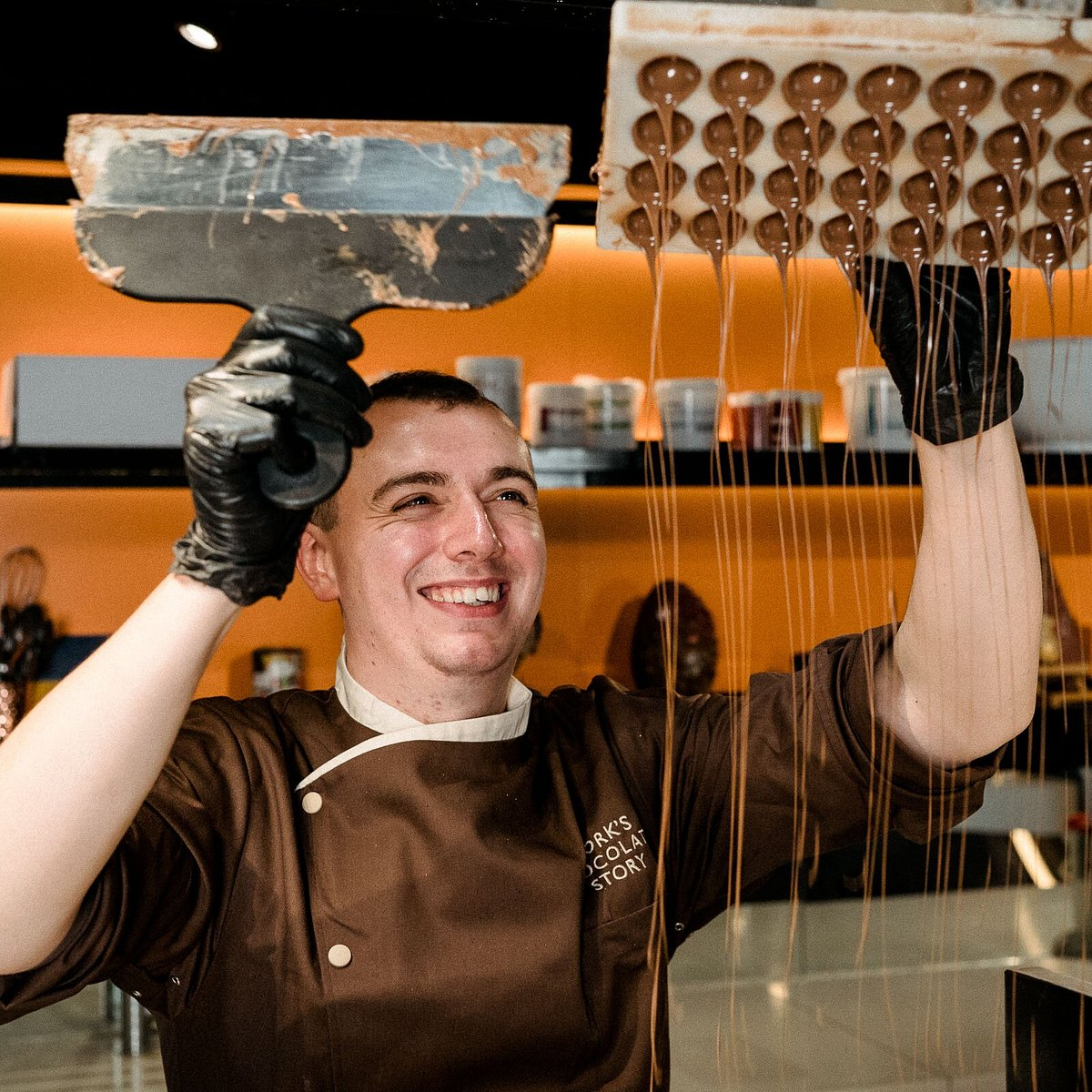 A man in a chef 's uniform is holding chocolate above his head