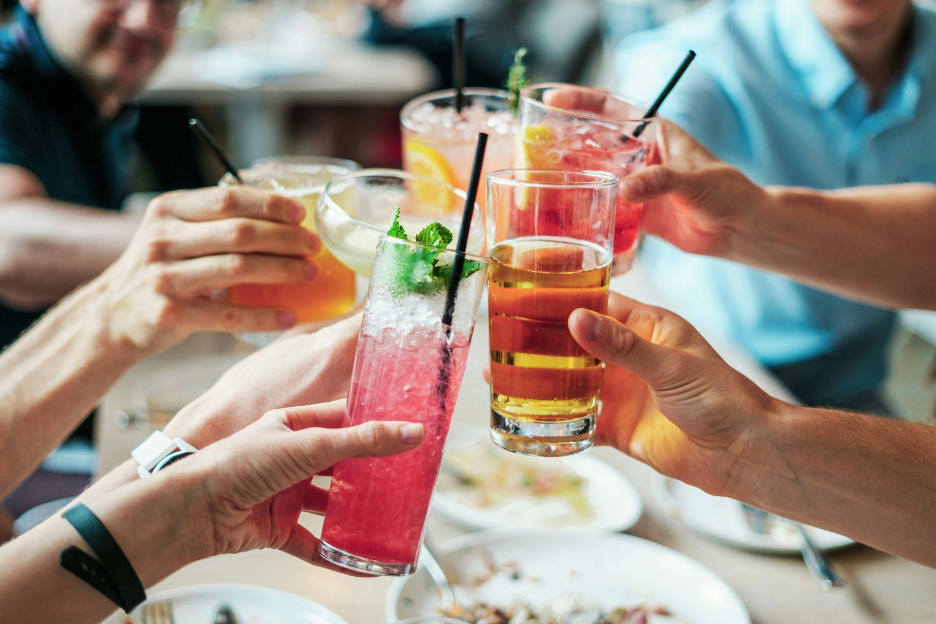 People toasting with colorful cocktails at an outdoor table.