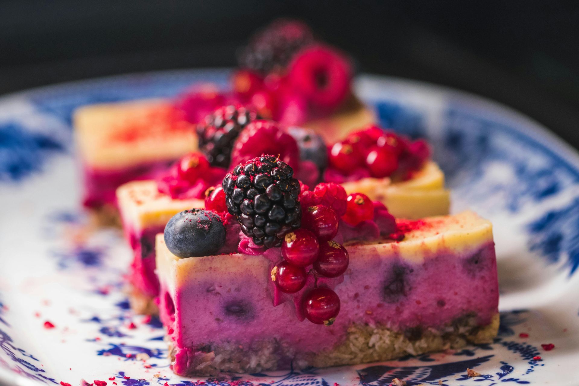 Berry cheesecake slices on a blue and white plate, topped with fresh berries.