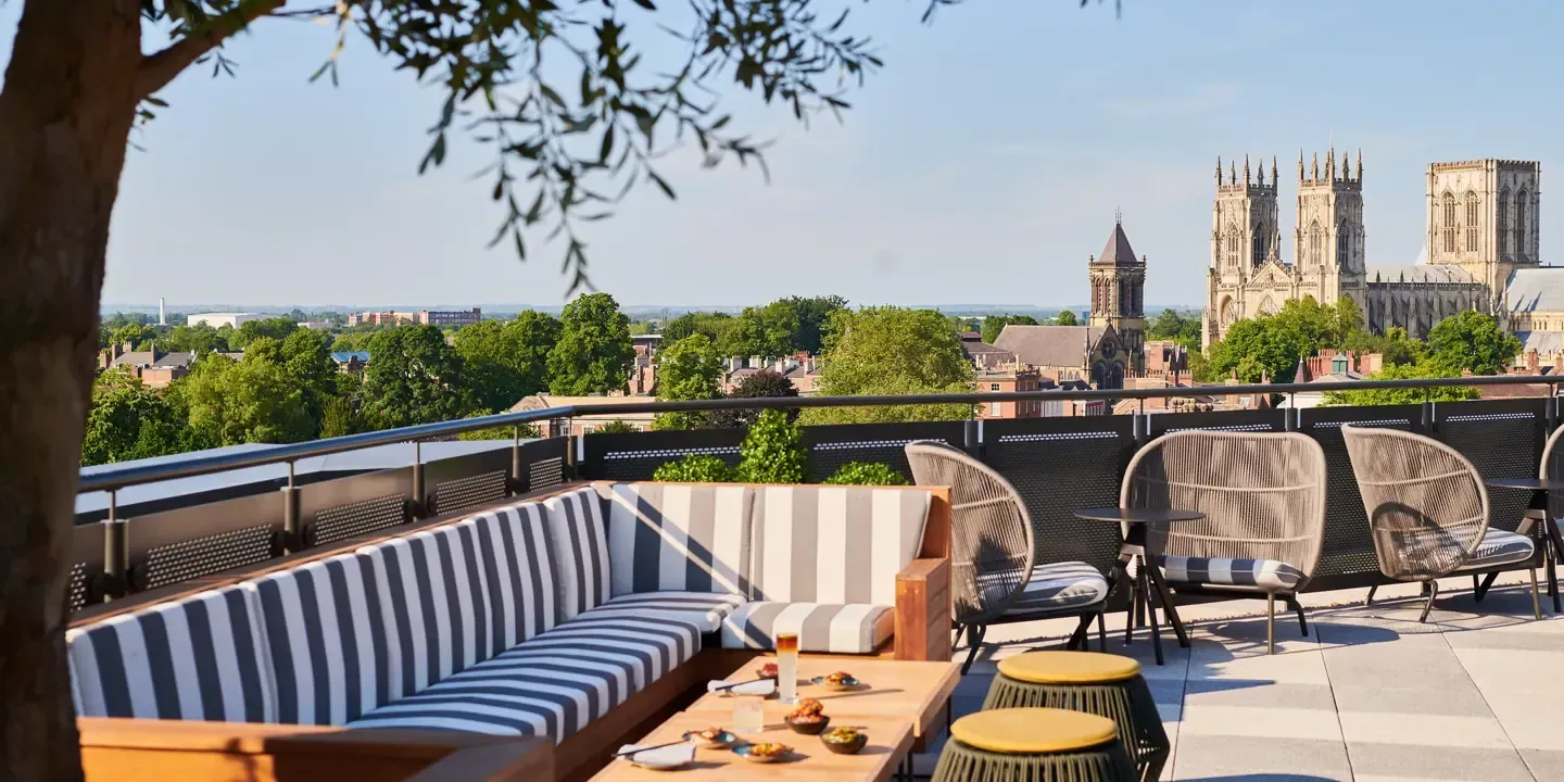 Rooftop lounge with striped seating and wicker chairs, overlooking a city with church towers.