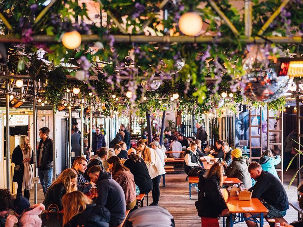 People at an outdoor dining area under floral decorations, string lights, and disco balls.