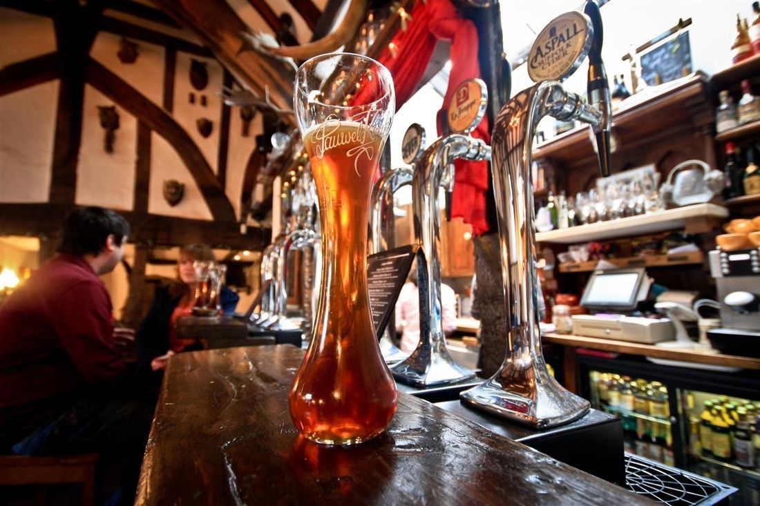 Tall glass of beer on a wooden bar in a pub, with taps in the background.