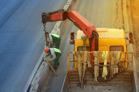 Dos obreros de la construcción trabajan en un muro junto a un camión con una grúa acoplada.