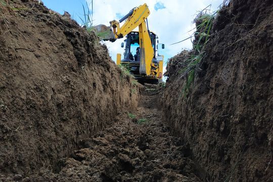Una excavadora amarilla está cavando una zanja en la tierra.