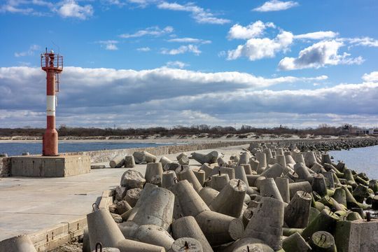 Un faro rojo y blanco está situado en la parte superior de un muelle al lado de un cuerpo de agua.