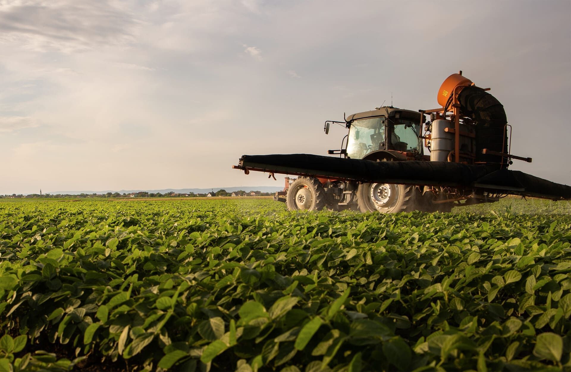 Pulverizador agrícola circulando por un campo de cultivo verde bajo un cielo despejado.
