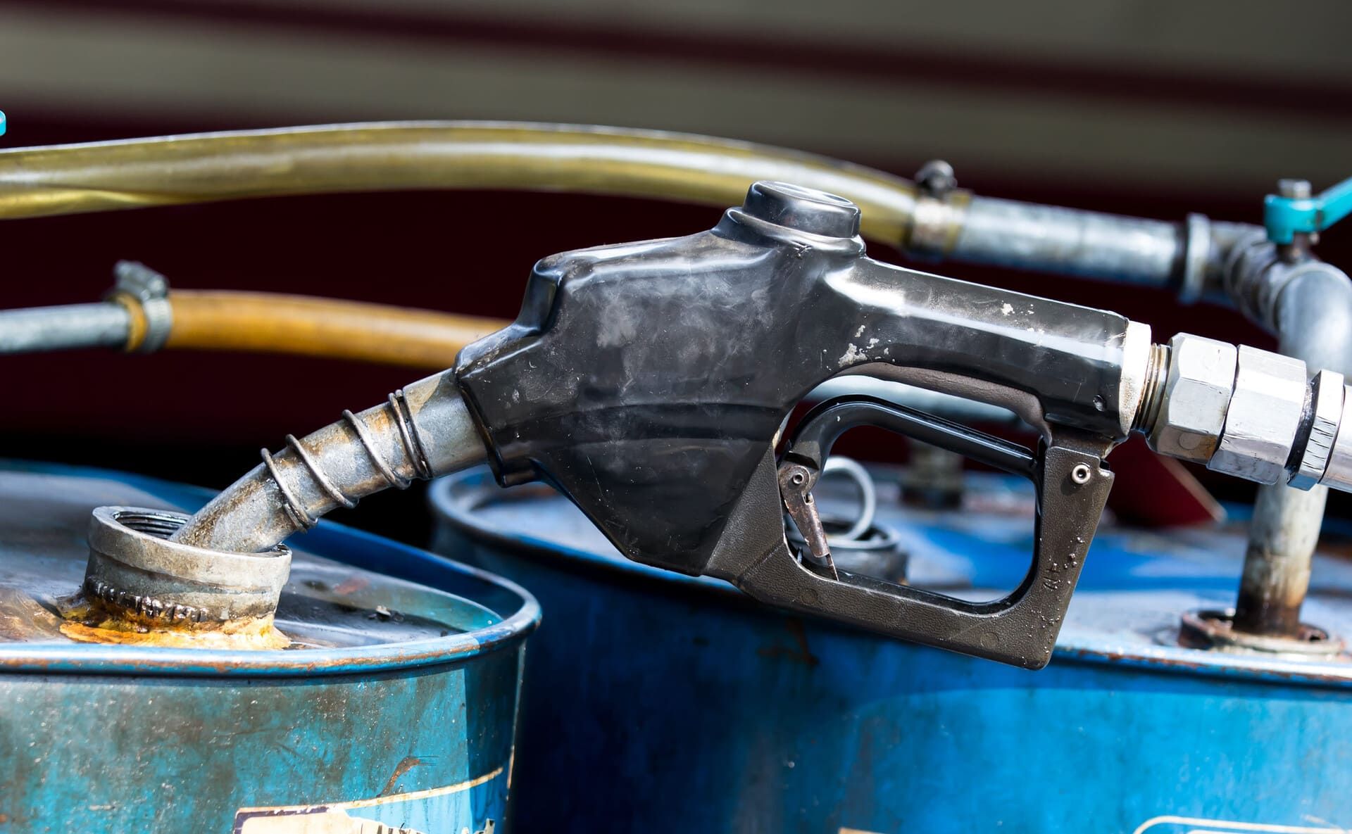 Boquilla de combustible insertada en un barril azul con mangueras conectadas en un sistema de almacenamiento de combustible.