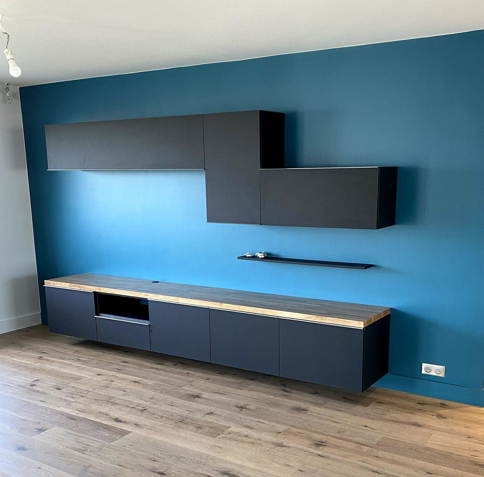Meuble de rangement mural noir sur un mur bleu moderne sur un sol en bois.