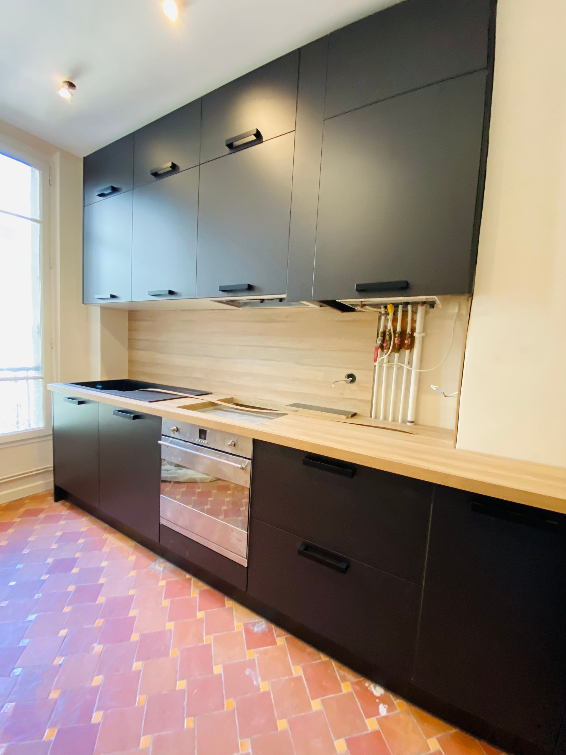 Une cuisine avec des meubles noirs et un mur vert foncé