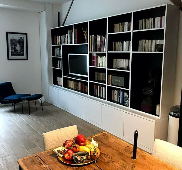 Bibliothèque encastrée blanche à intérieur noir, télévision et placards bas. 
