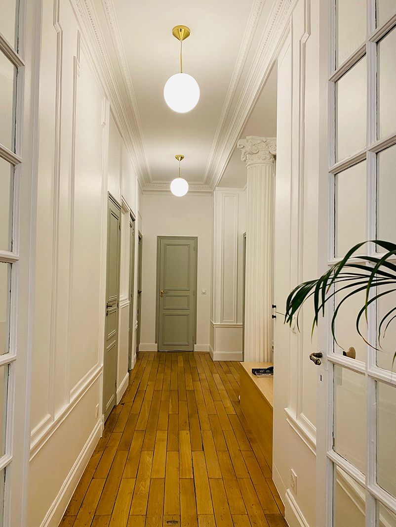 Un couloir avec plusieurs portes peintes en vert et du parquet au sol