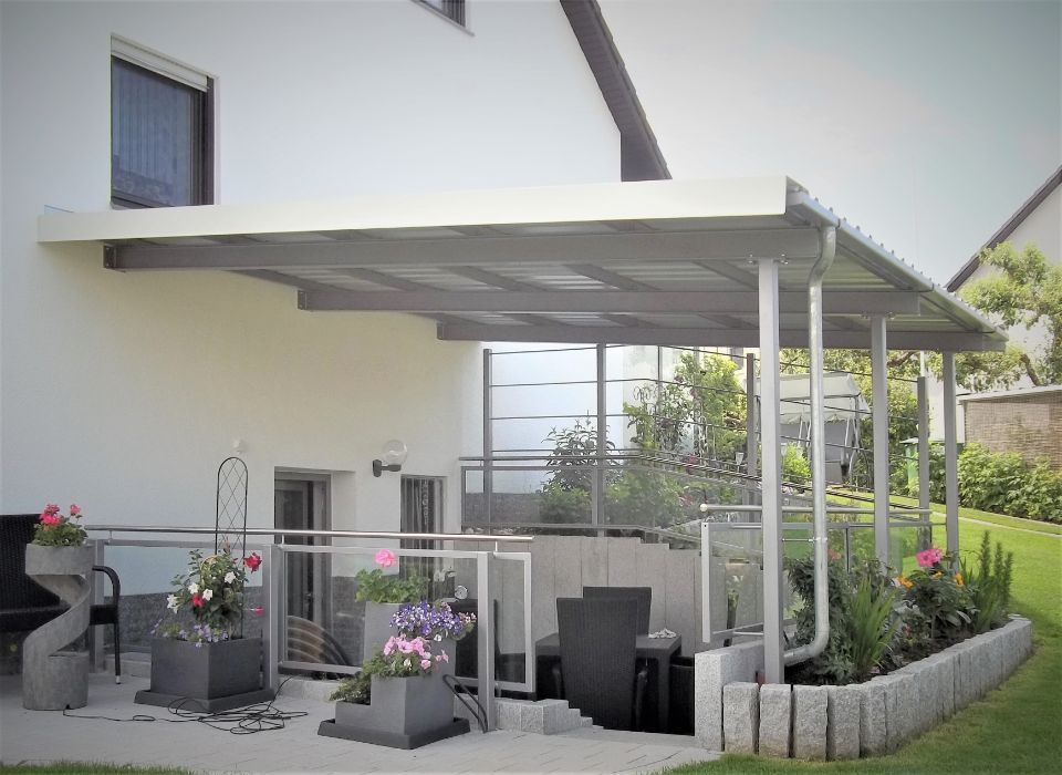 Terrasse mit Geländern und Gartenmöbeln, die von einer Überdachung überspannt wird
