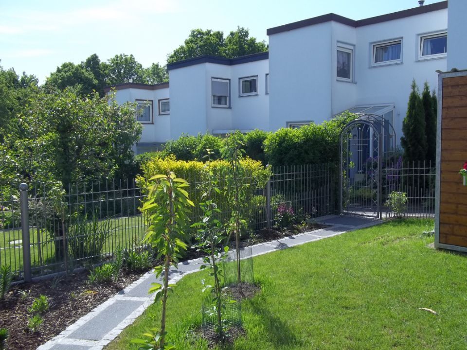 Gartenanlage mit Rasenfläche, Bäumen, Weg und Gartenzaun mit hohem Tor