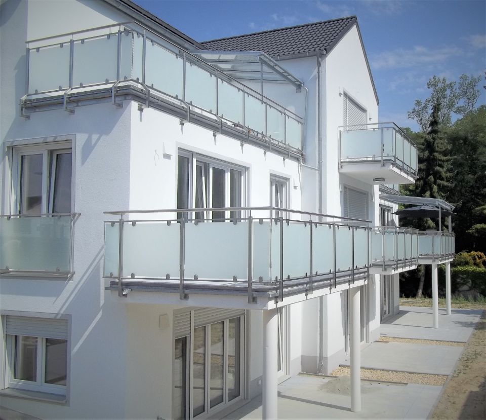 Mehrere Balkone an einem weißen Haus mit Geländern aus Milchglasscheiben und Metallrahmen