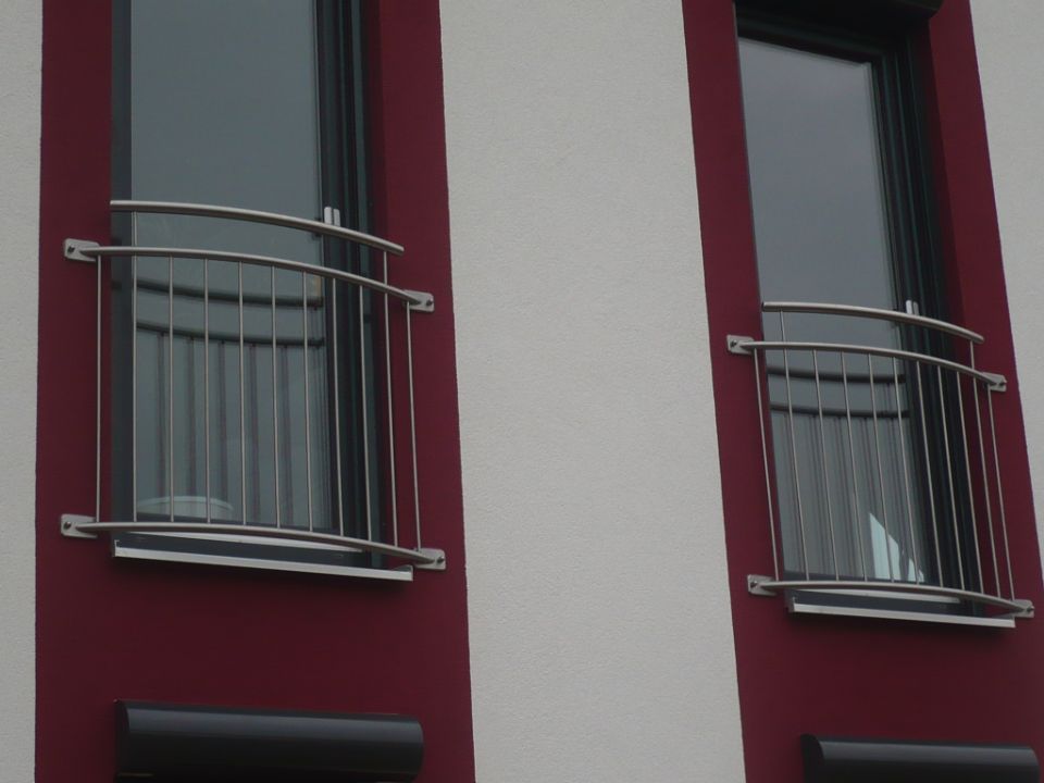 Zwei Balkongeländer vor bodenlangen Fenstern