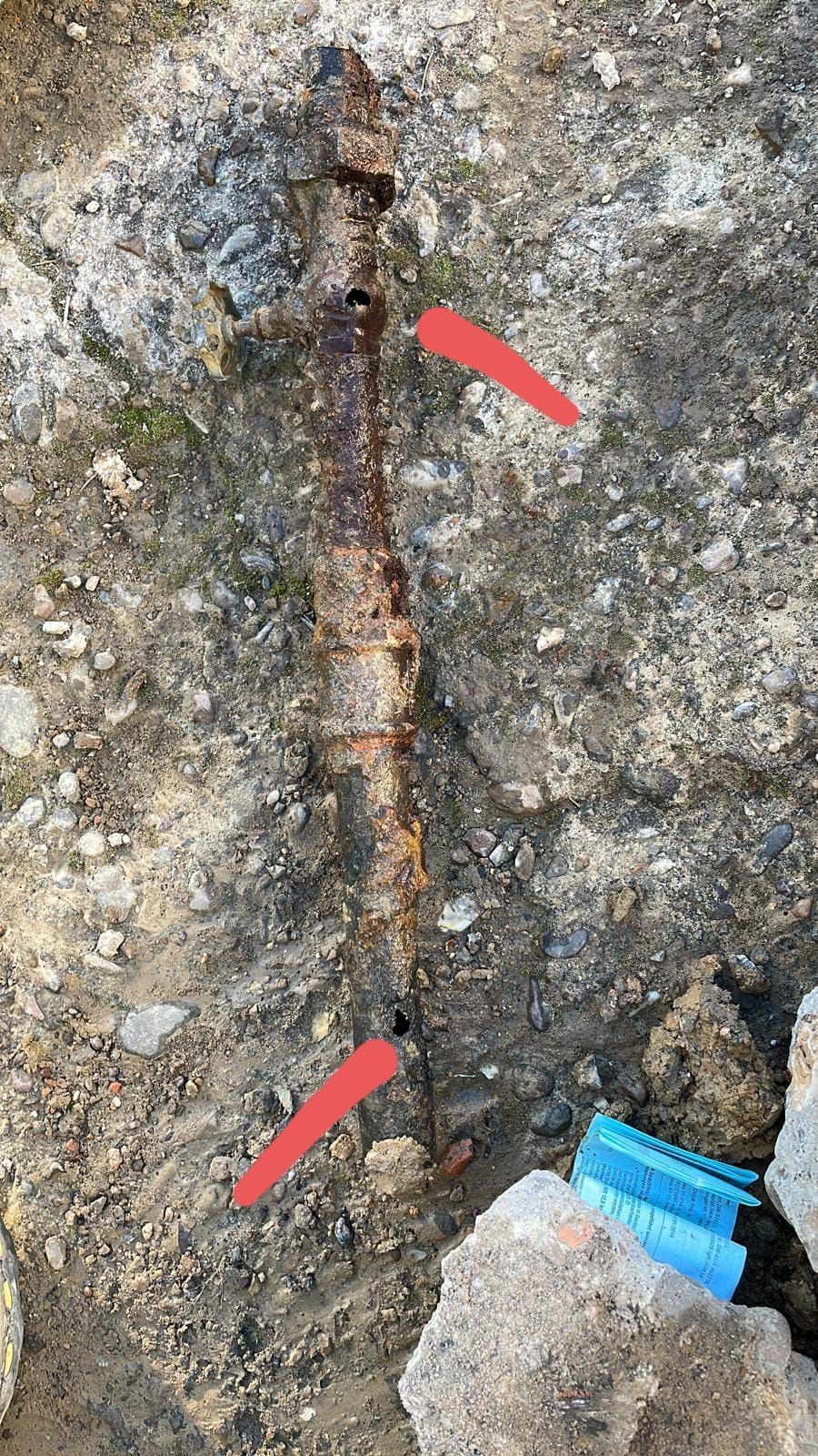 Hay una tubería oxidada en el suelo con flechas rojas apuntando hacia ella.
