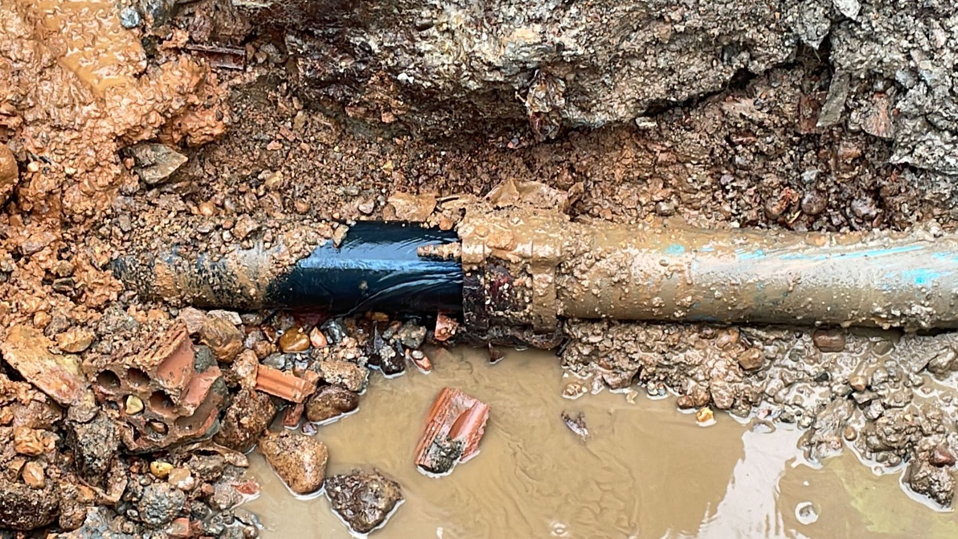 Una tubería rota yace en la tierra al lado de un charco de agua.