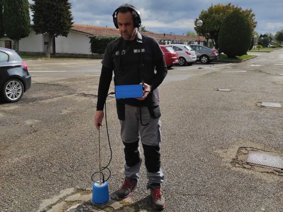 Un hombre que lleva auriculares está parado en un estacionamiento sosteniendo una caja azul.