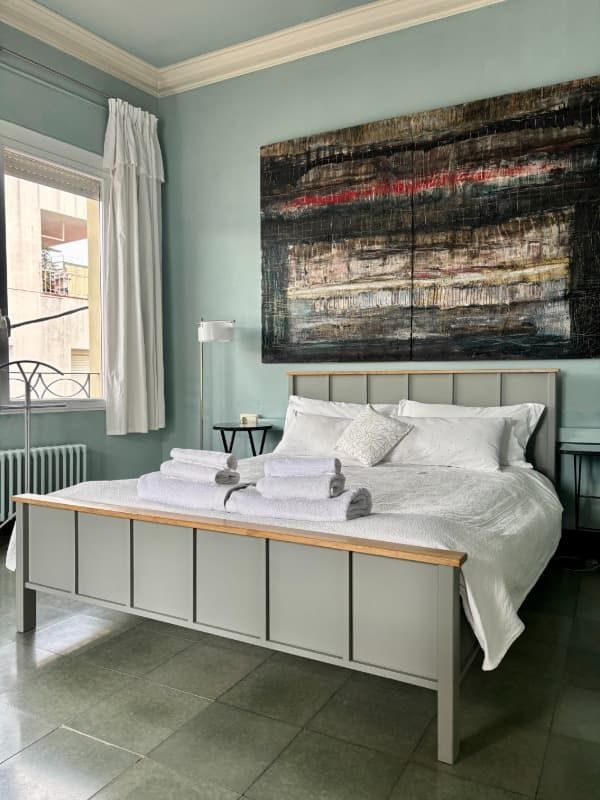 Dormitorio moderno con una cama bien hecha, arte abstracto en la pared y paredes de color verde suave.