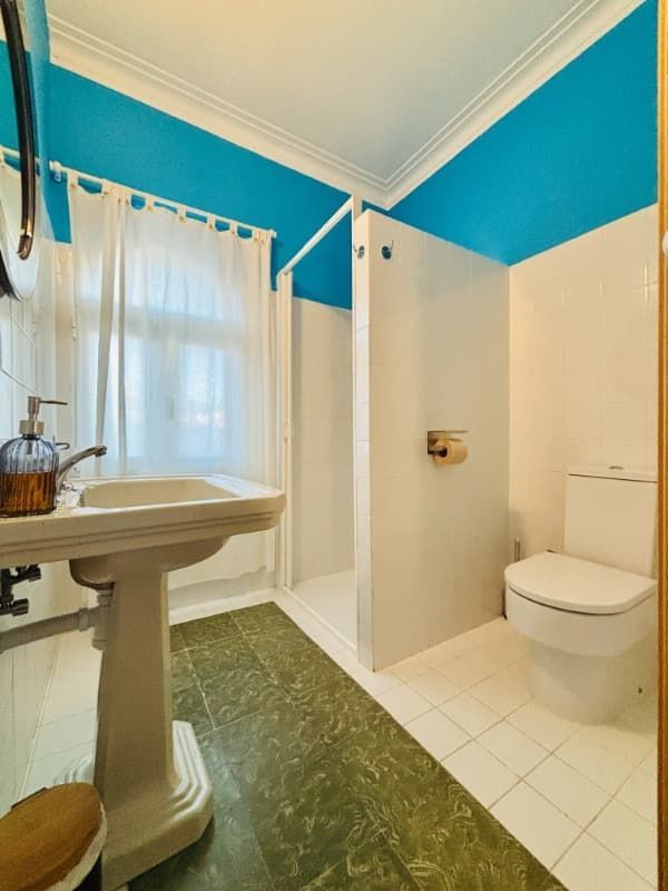 Baño luminoso con lavabo de pedestal, cortina de ducha, inodoro y paredes de color verde azulado.