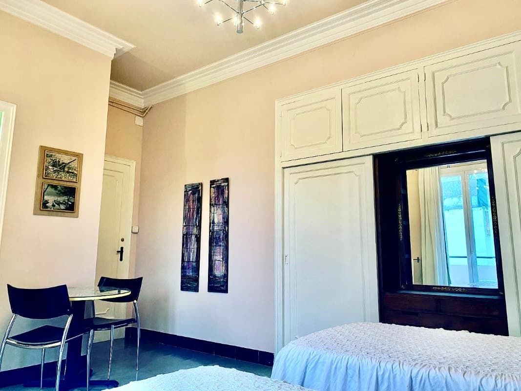 Habitación pequeña con armarios empotrados blancos, una cama, sillas de escritorio y cuadros enmarcados en tonos crema.