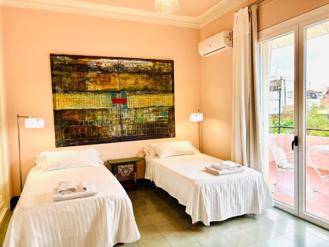 Habitación luminosa con dos camas individuales, cuadros en la pared y una puerta corredera de cristal que da a un patio.