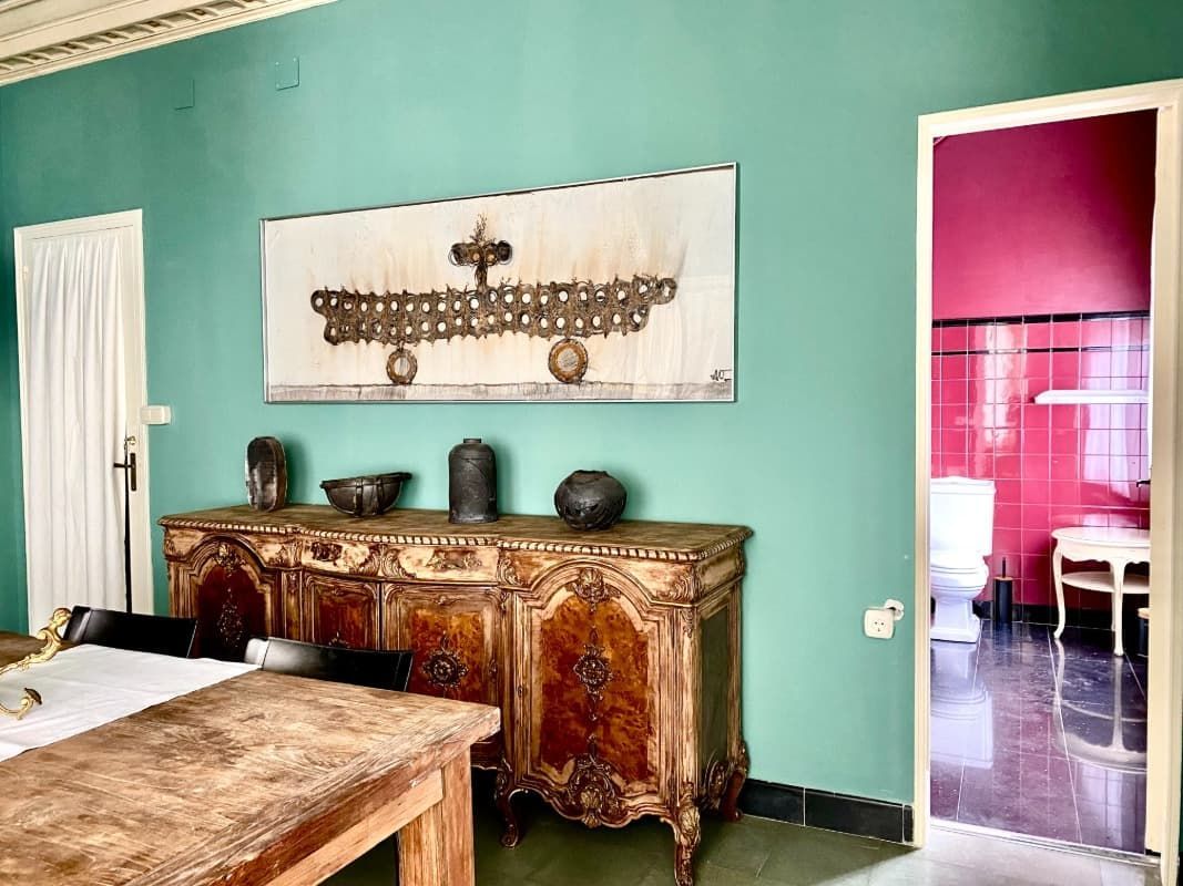 Habitación con paredes turquesas, armario de madera ornamentado, mesa y puerta que da a una habitación rosa.