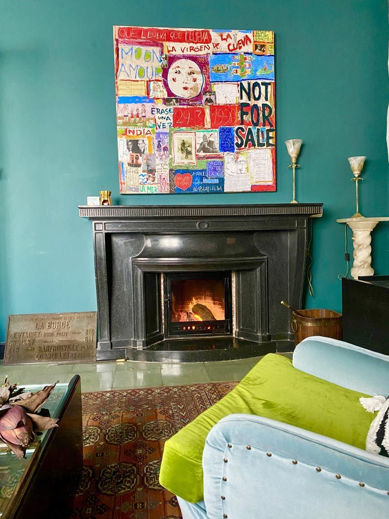 Sala de estar con paredes color turquesa, chimenea negra, obras de arte coloridas y una silla azul con una manta verde lima.