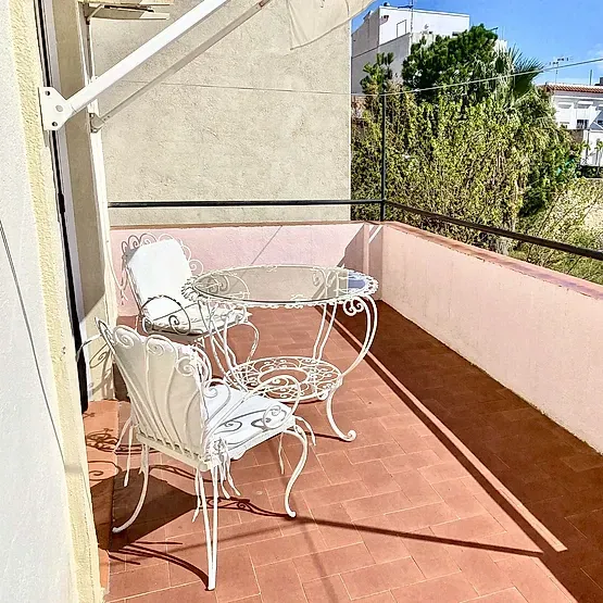 Balcón soleado con mesa y sillas de hierro forjado blanco sobre baldosas de terracota.