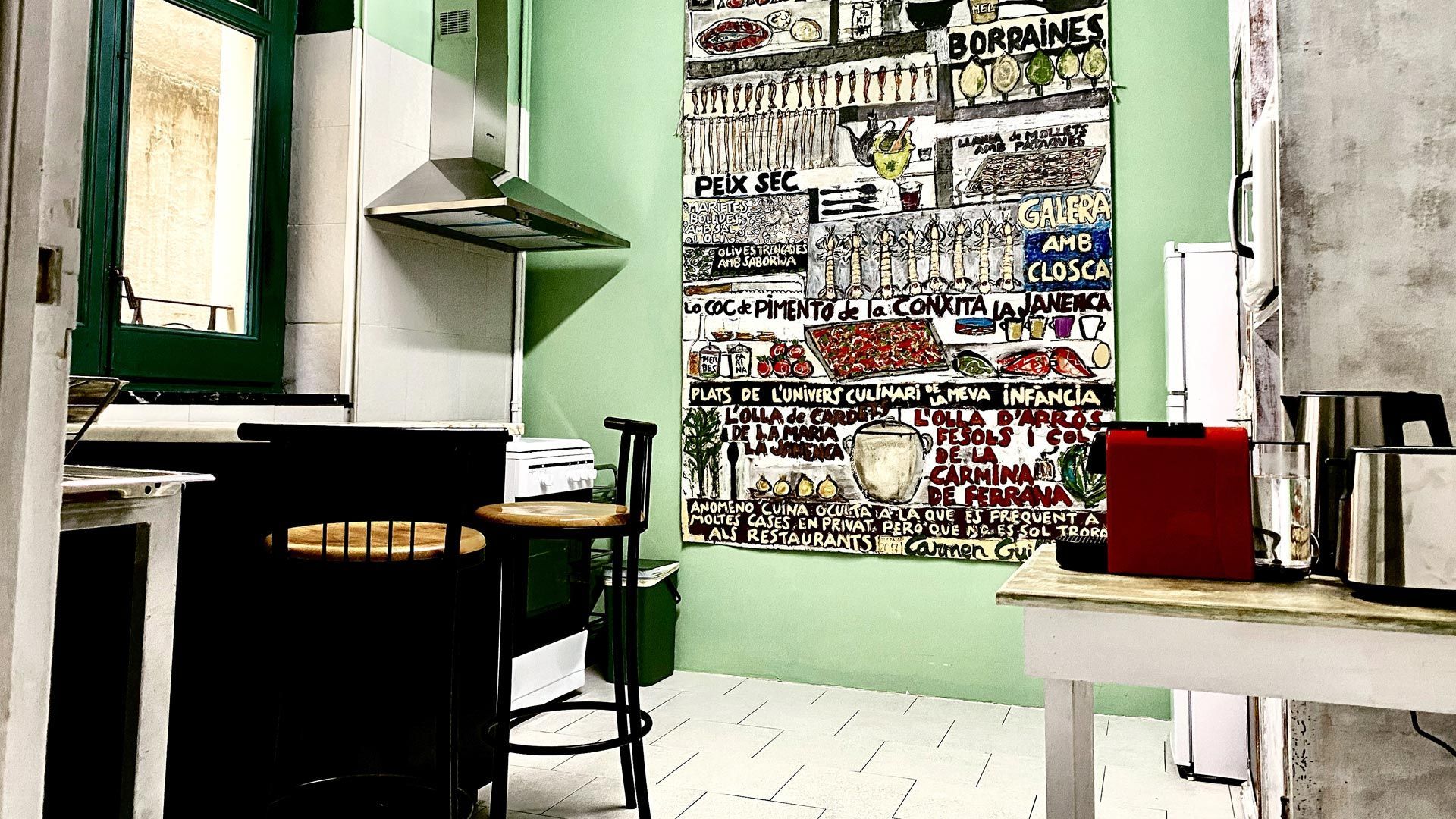 Cocina moderna con paredes verdes, sillas negras, mesa blanca y una pared cubierta de collage.