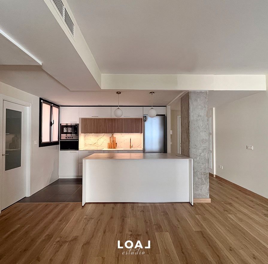 Cocina y sala de estar de un apartamento moderno y vacío, con suelos de madera y armarios blancos