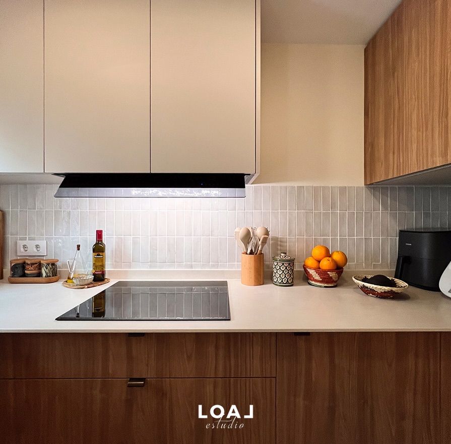 Cocina moderna con armarios de madera, encimeras blancas, placa de cocina y un cuenco de naranjas sobre la encimera