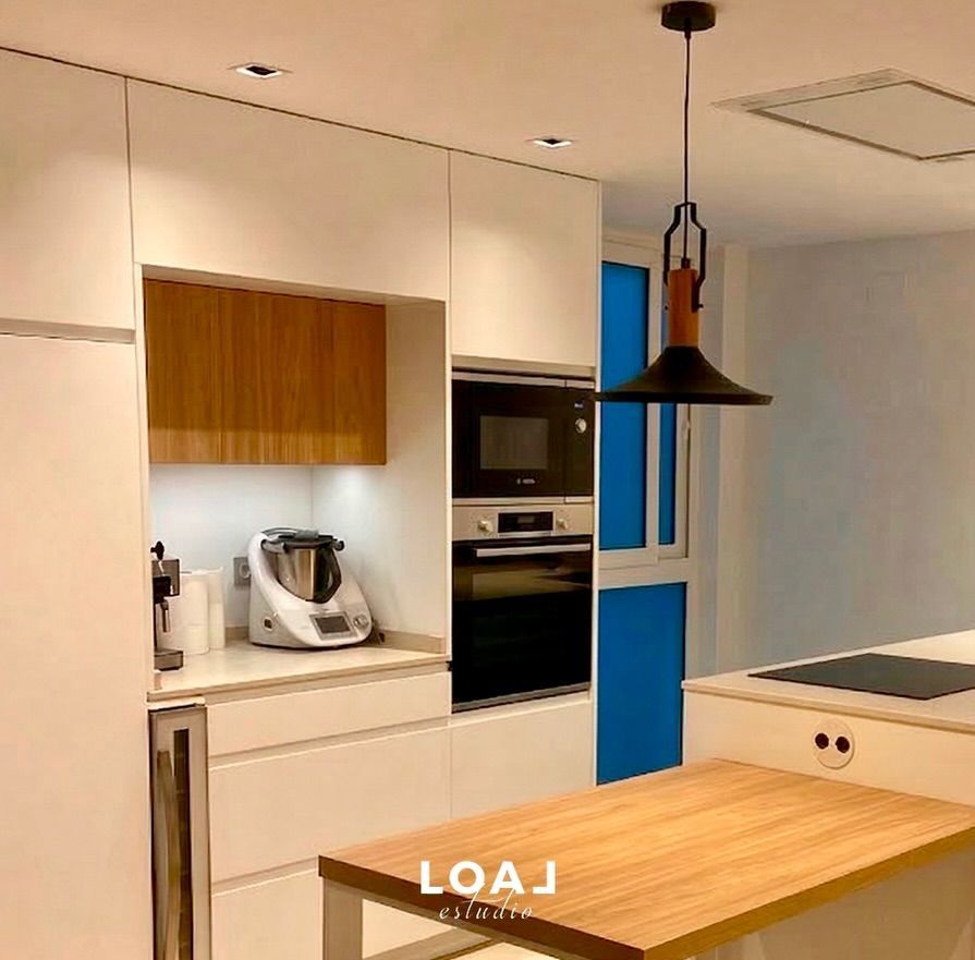 Cocina moderna con armarios blancos, detalles de madera, isla y lámpara colgante negra