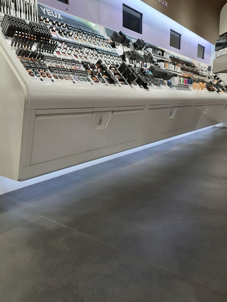Allée de magasin moderne avec un long comptoir blanc et des étagères présentant du maquillage sous un éclairage vif.
