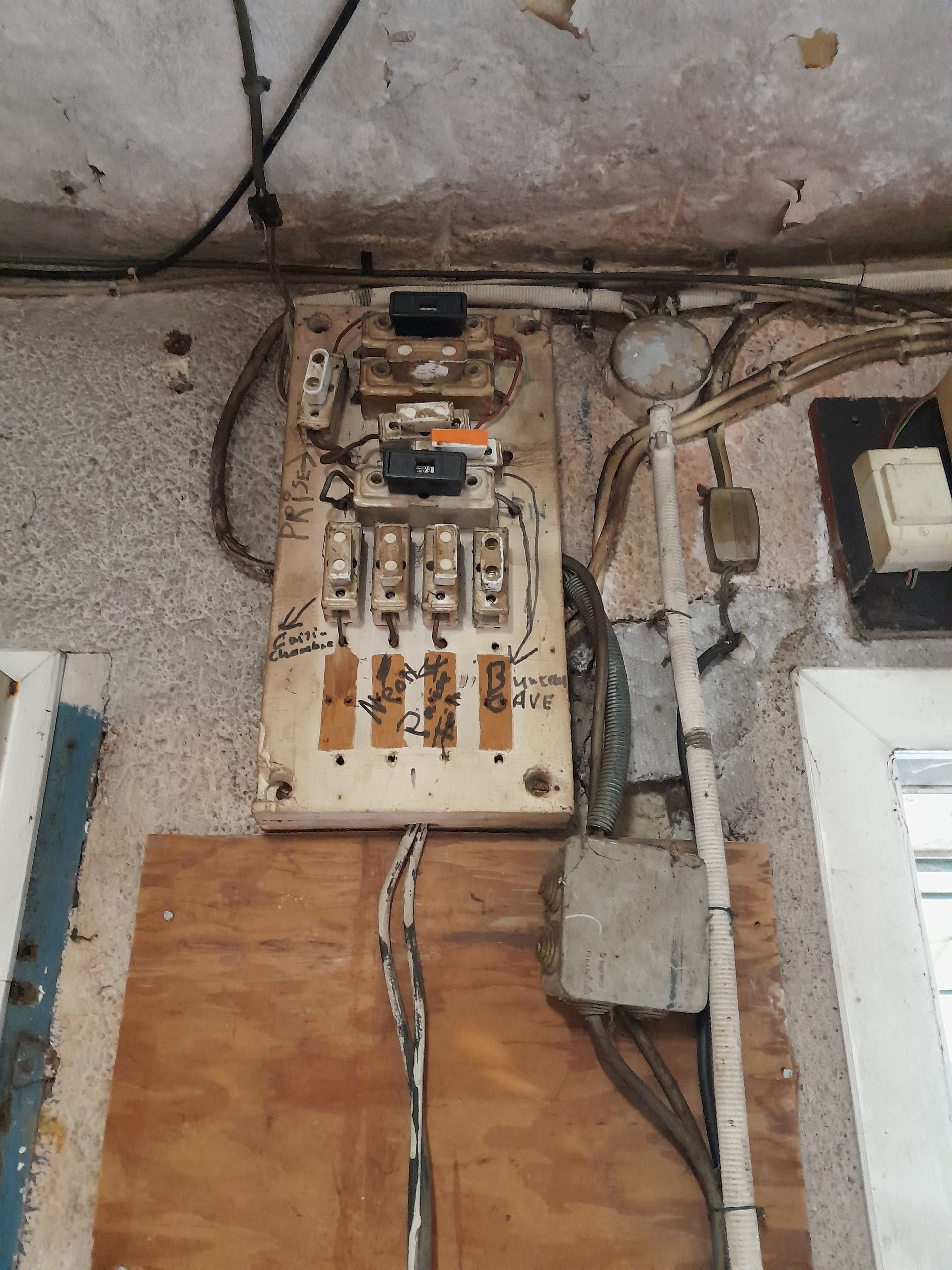 Ancien tableau électrique avec fils apparents sur un mur.