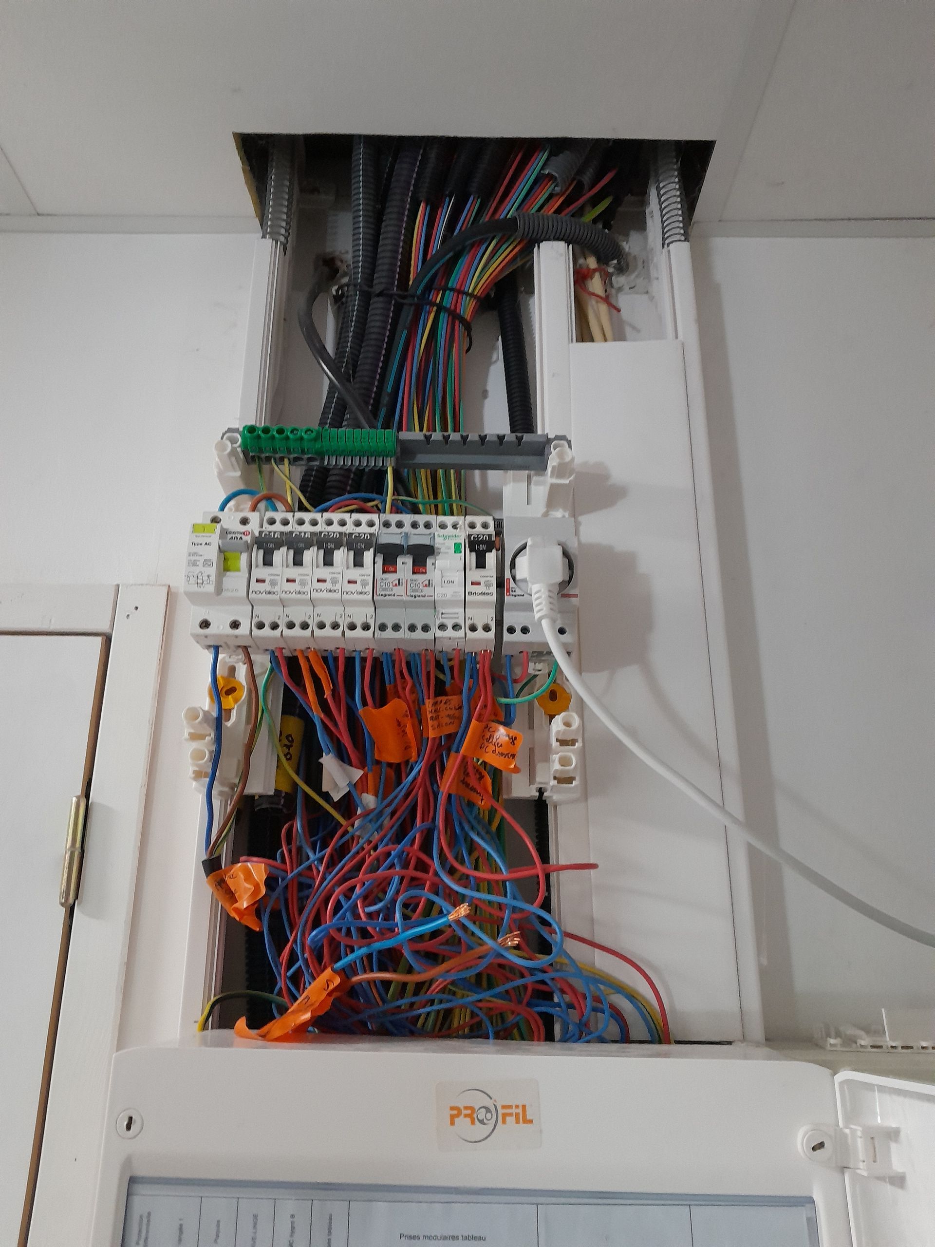 Tableau électrique ouvert avec des fils multicolores et des disjoncteurs dans une armoire murale.