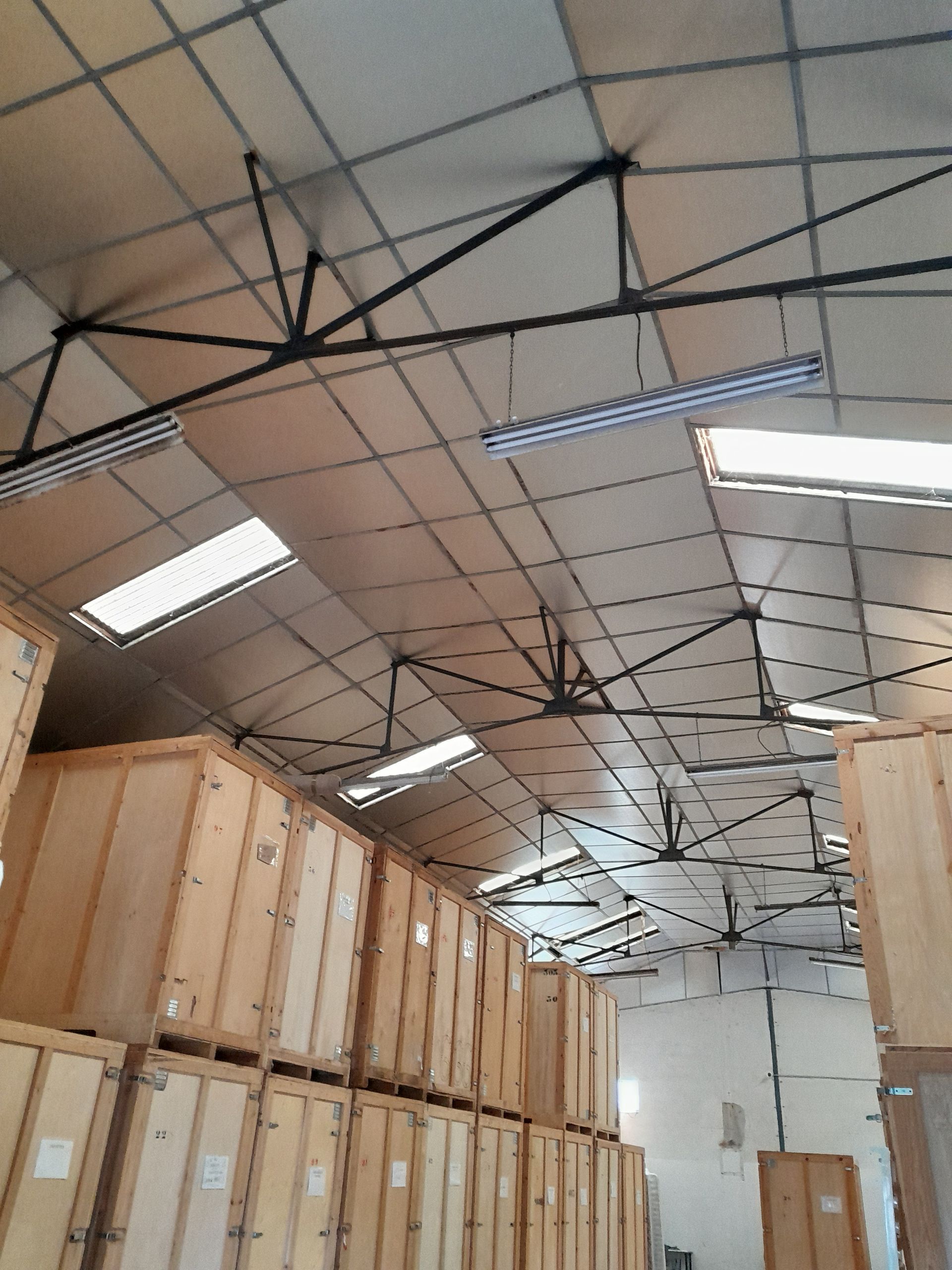 Intérieur d'entrepôt avec des caisses en bois empilées et un haut plafond équipé d'éclairages.