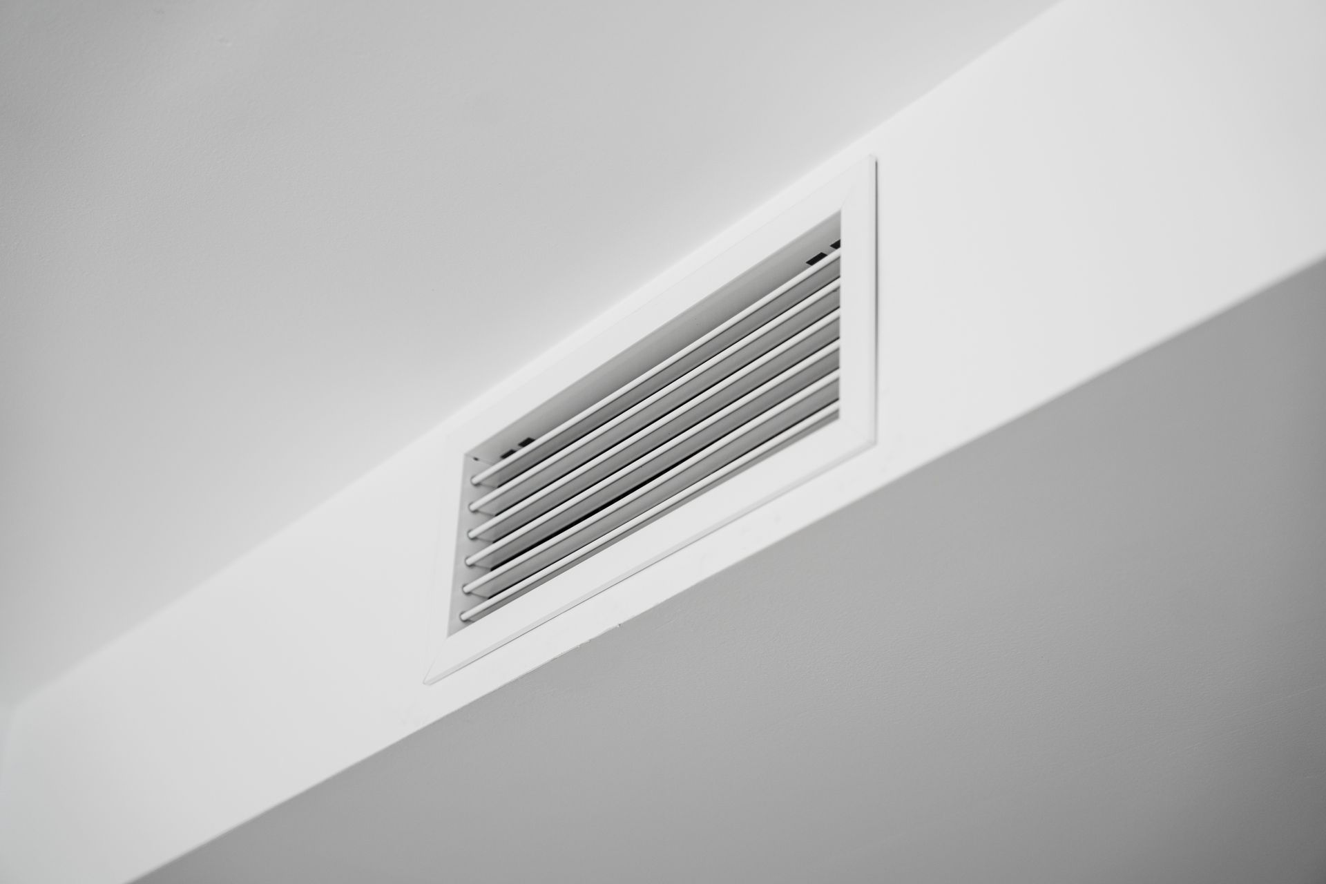 Grille d'aération blanche près du plafond sur un mur intérieur.